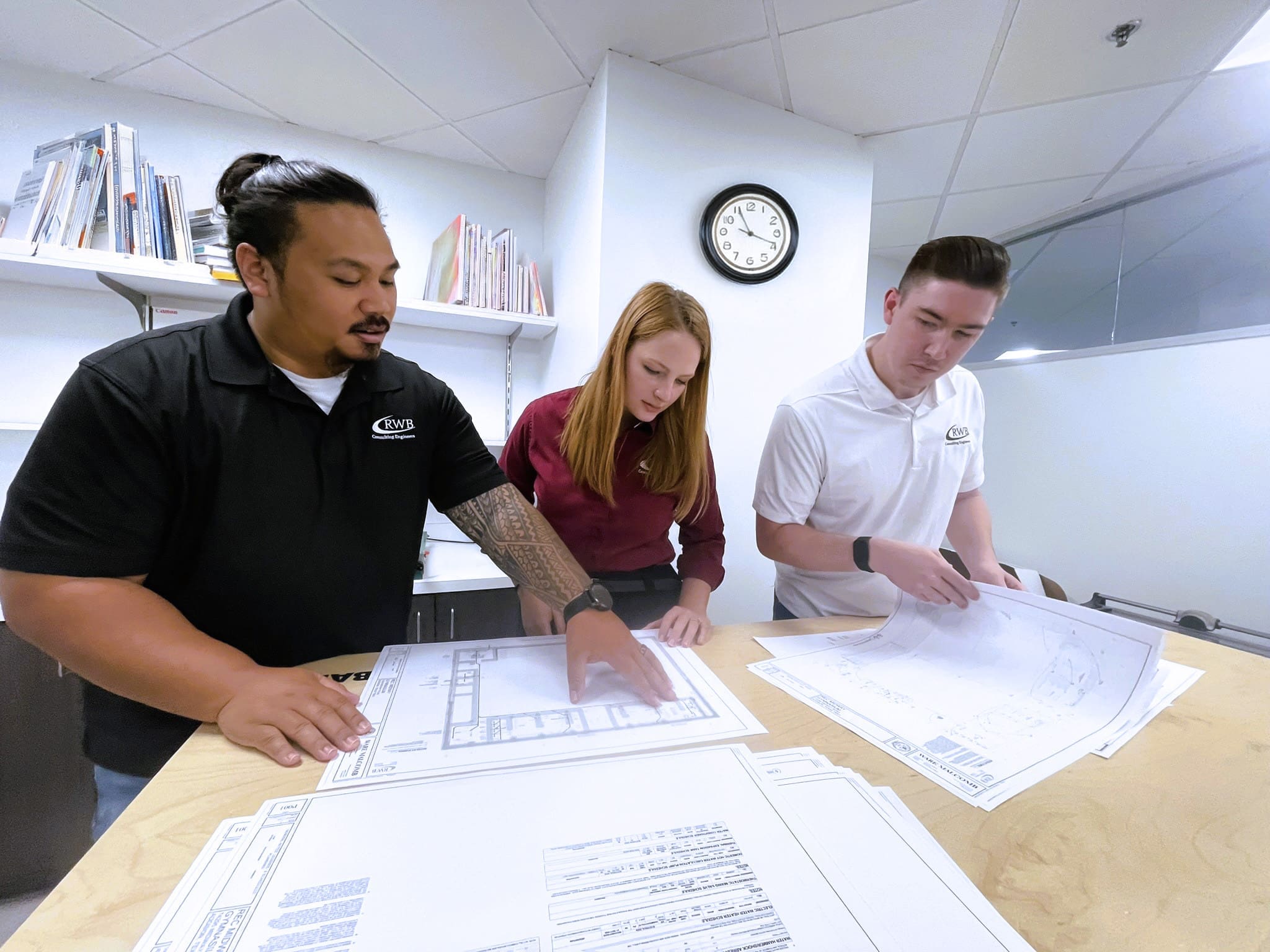 Three engineers review paper drawings on a table.